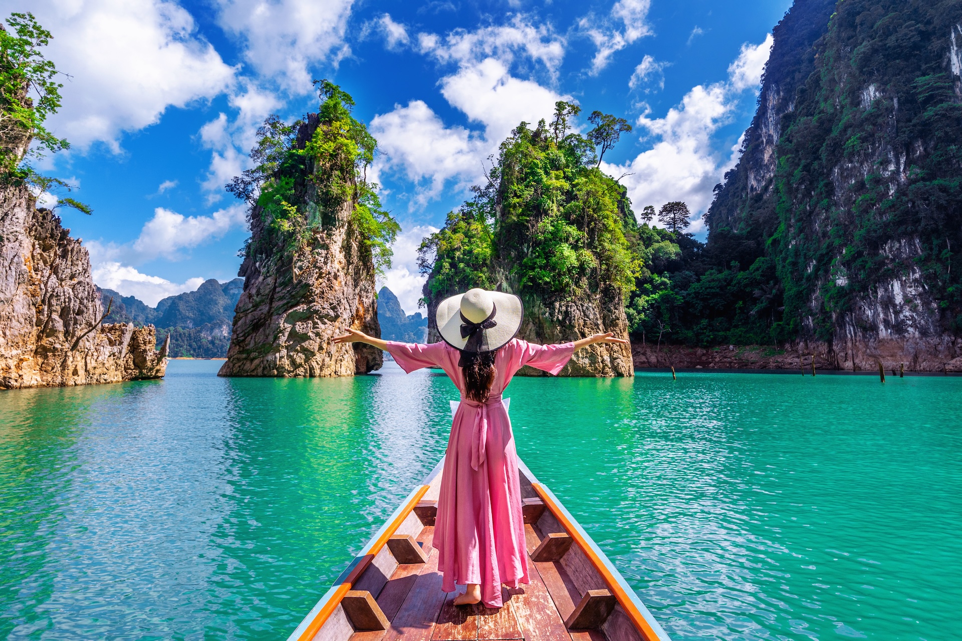 Beautiful girl standing on the boat and looking to mountains in ratchaprapha dam at khao sok national park, surat thani province, thailand.